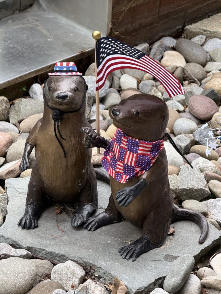 Two otter statues on rocks&mdash;one in a patriotic hat, the other with a USA flag-themed bandana and holding a small American flag&mdash;make for a fun photo spot and one of the unique things to do in Fredericksburg with kids.