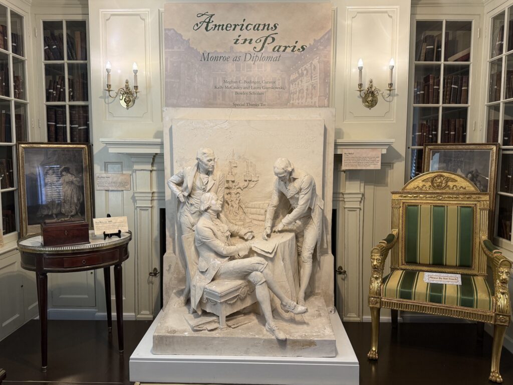 A museum display titled &ldquo;Americans in Paris: Monroe as Diplomat,&rdquo; featuring a white sculpture of four men, period furniture, framed pictures, and informational plaques, highlights the lasting influence of Fredericksburg&rsquo;s own James Monroe on international diplomacy.