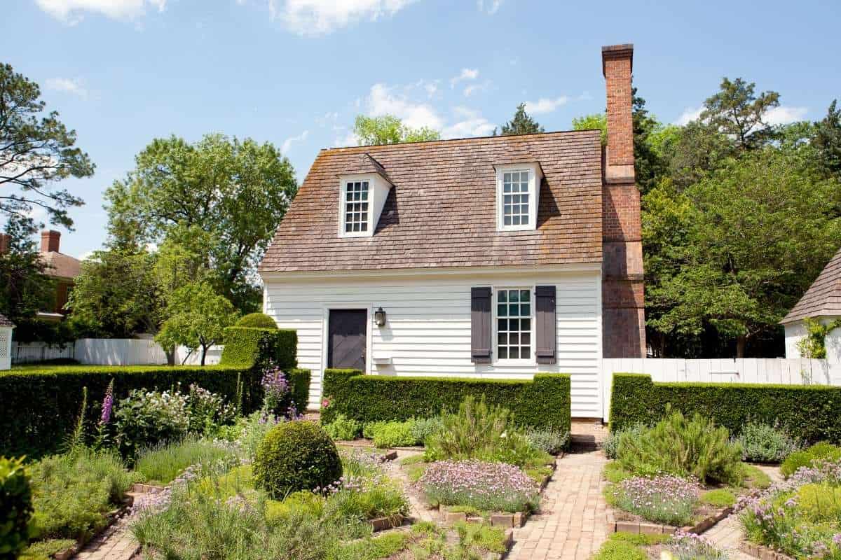 small white colonial cottage with formal gardens in front