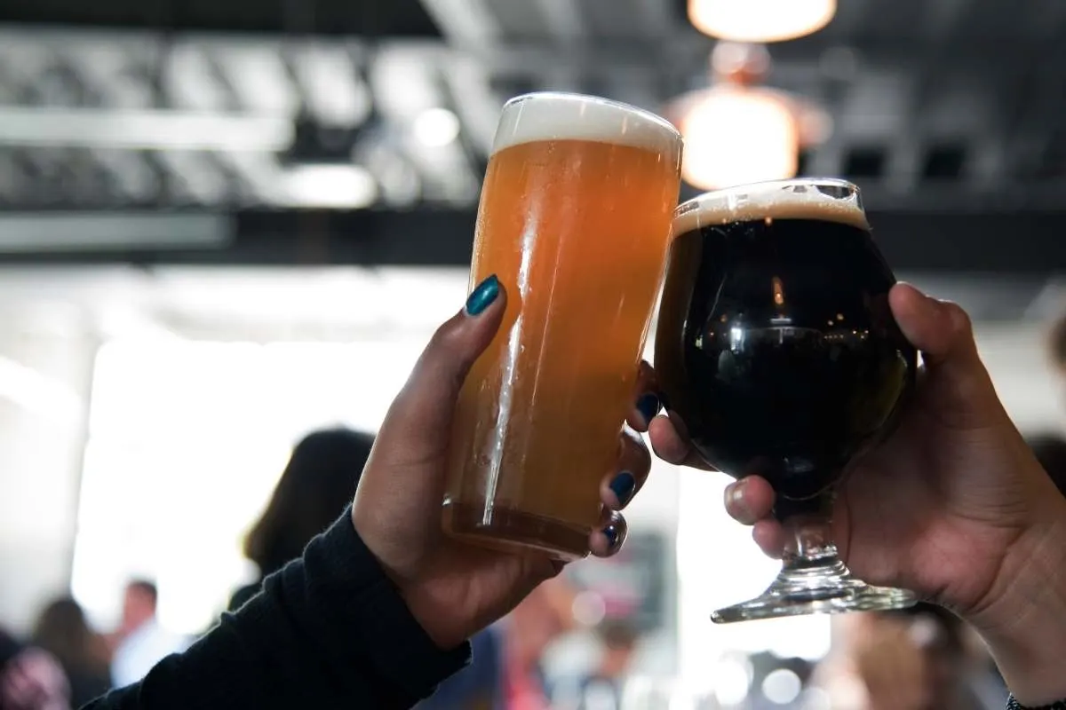 2 hands in crowded tasting room holding glasses of beer