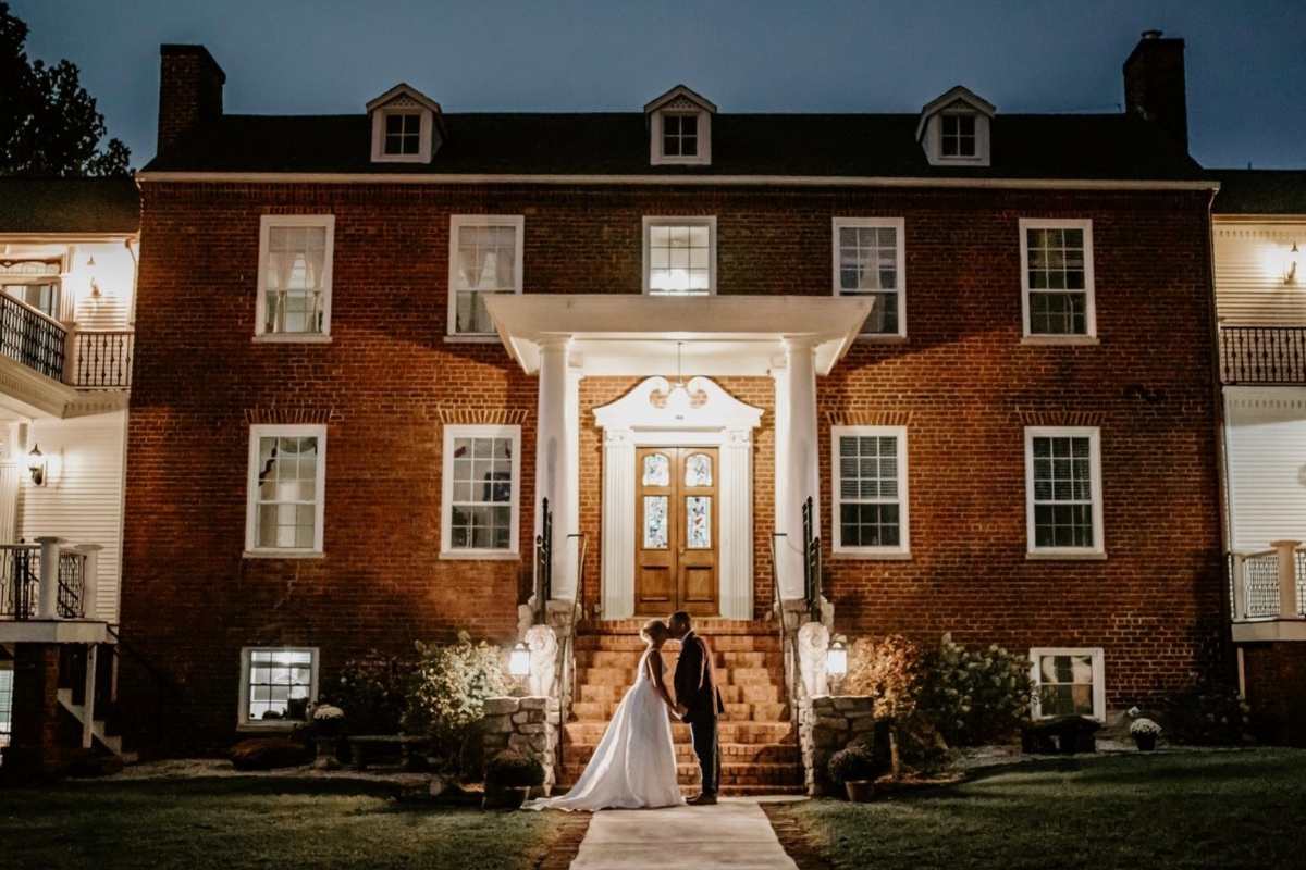 historic brick manor home at night with bride and groom on front steps
