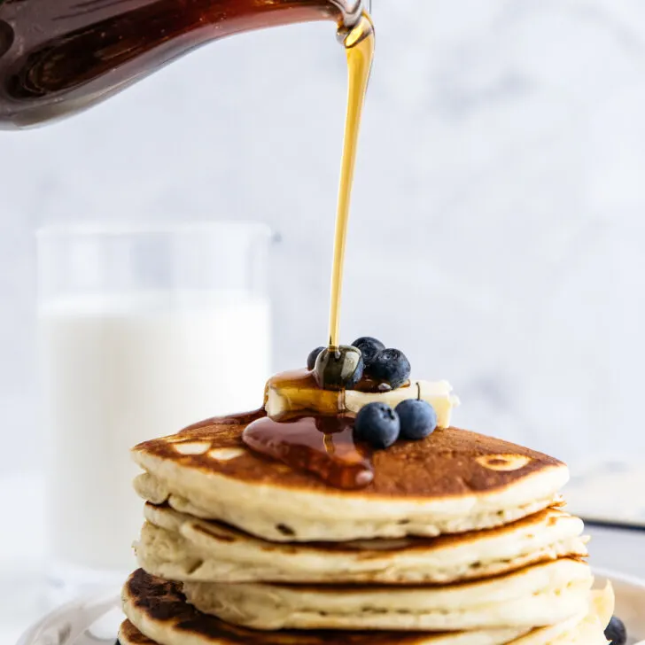 A stack of pancakes being poured with Fredericksburg syrup.