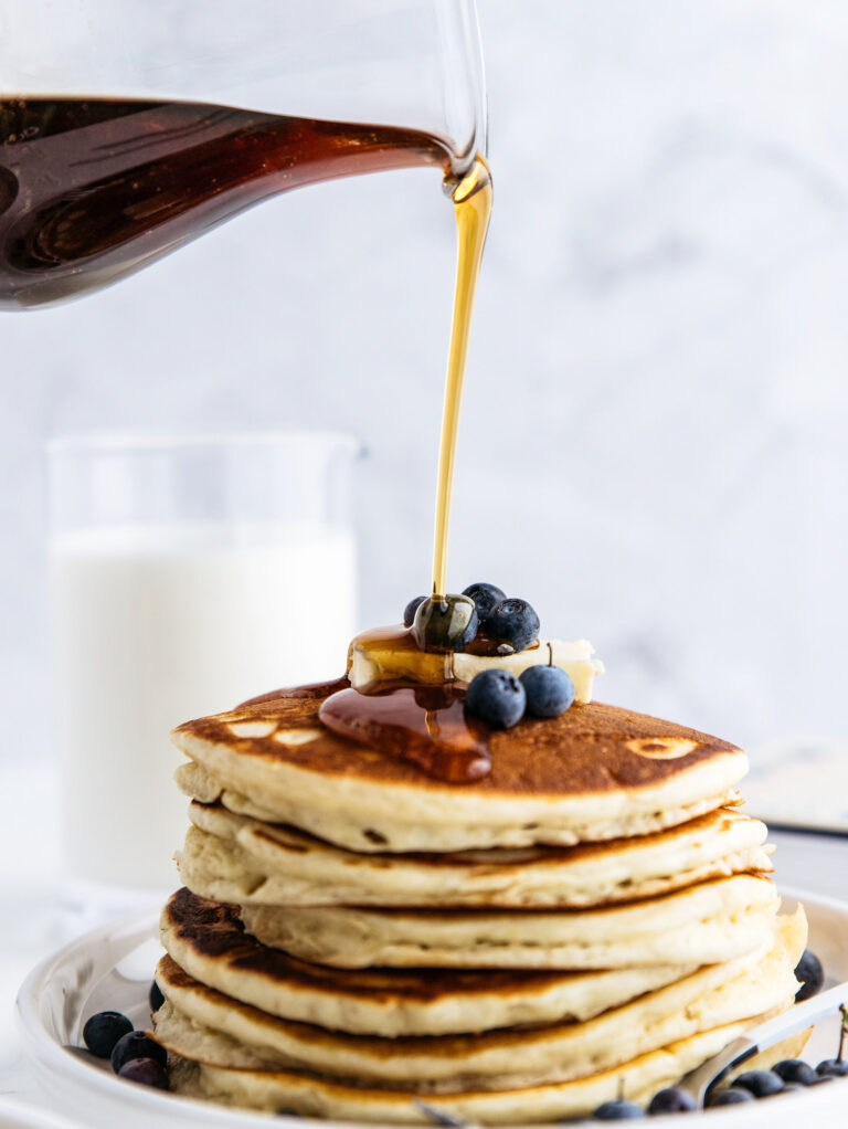A stack of pancakes being poured with Fredericksburg syrup.