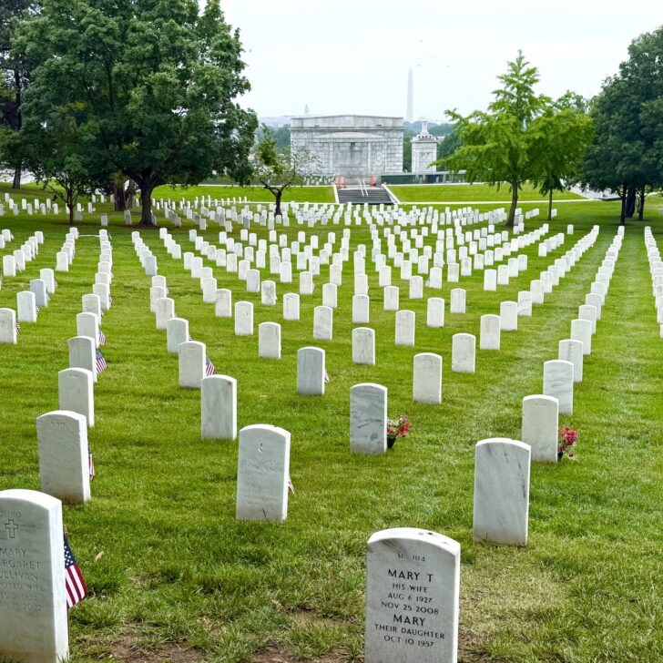 Rows of white gravestones in a green cemetery with trees and distant monuments visible in the background—an evocative spot often included on day trips from northern Virginia.