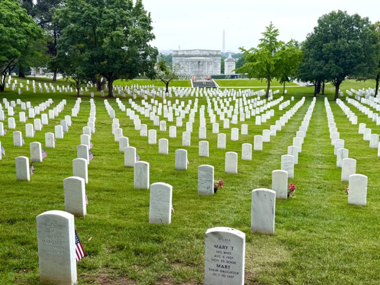 Rows of white gravestones in a green cemetery with trees and distant monuments visible in the background—an evocative spot often included on day trips from northern Virginia.