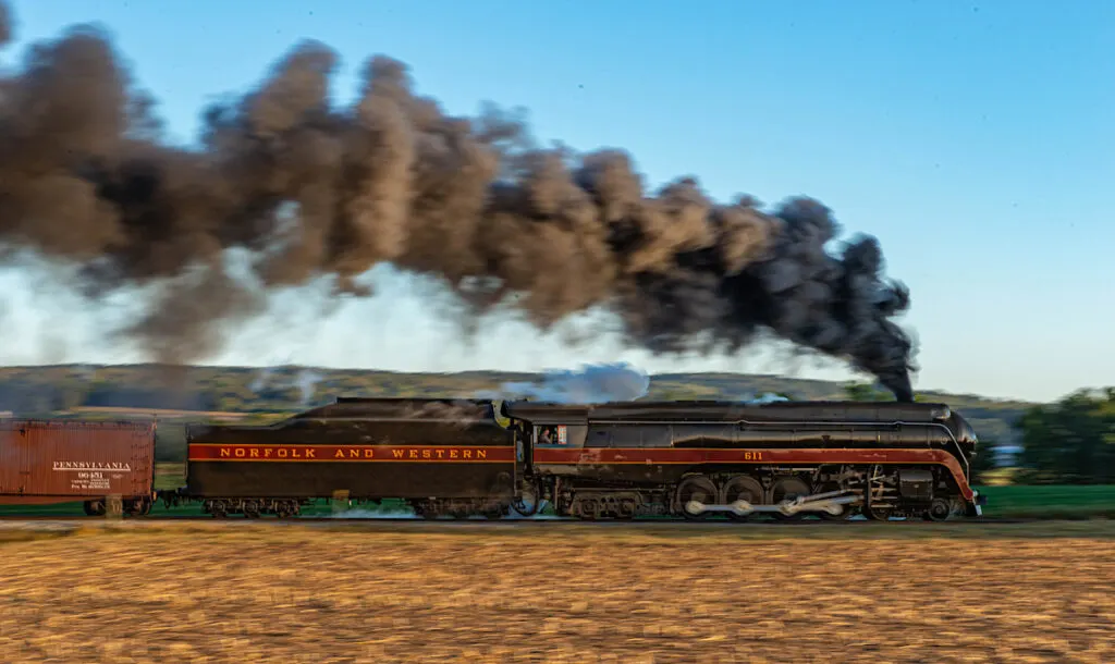 Norfolk and Western no. 611 is coming down a track through farmland with dark black smoke billowing.