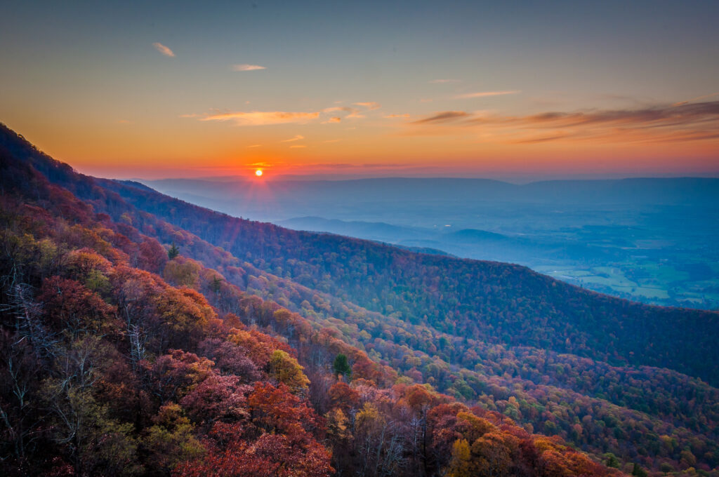 The sun is setting over a valley with colorful trees.