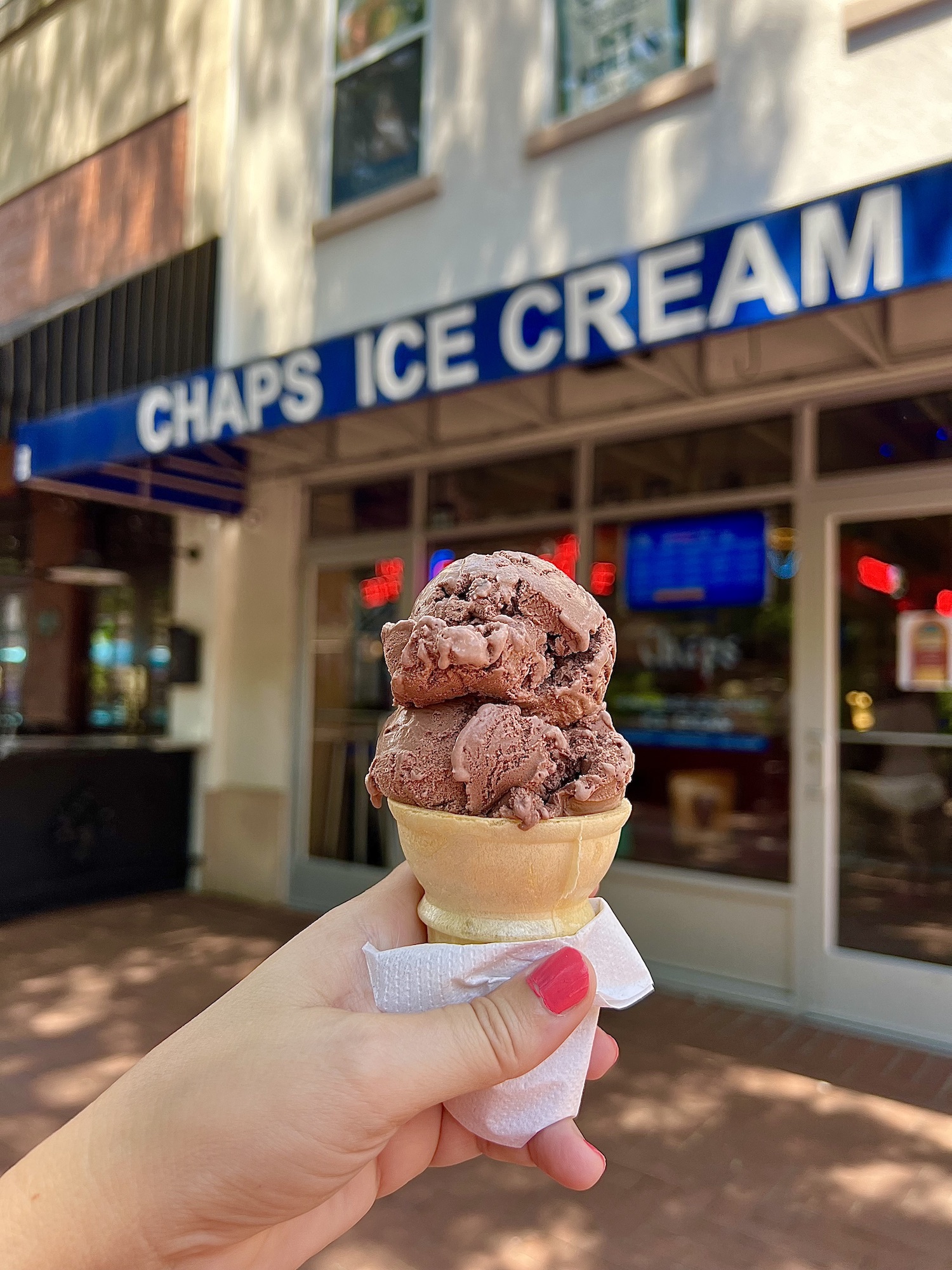 A person holding up a cone of ice cream in front of the chaps ice cream shop.