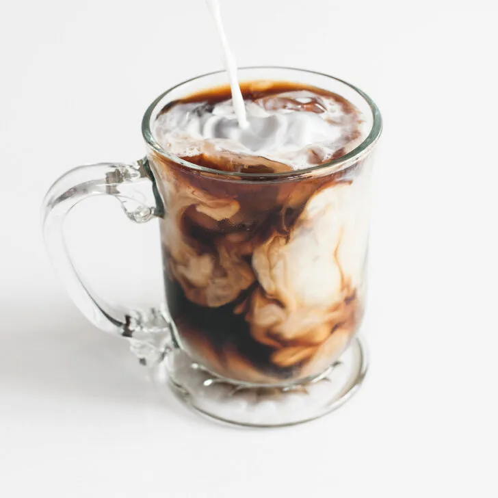 An iced coffee is being poured into a glass cup.
