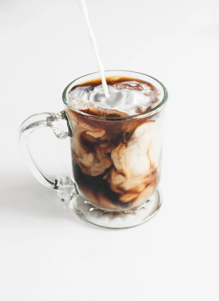 An iced coffee is being poured into a glass cup.