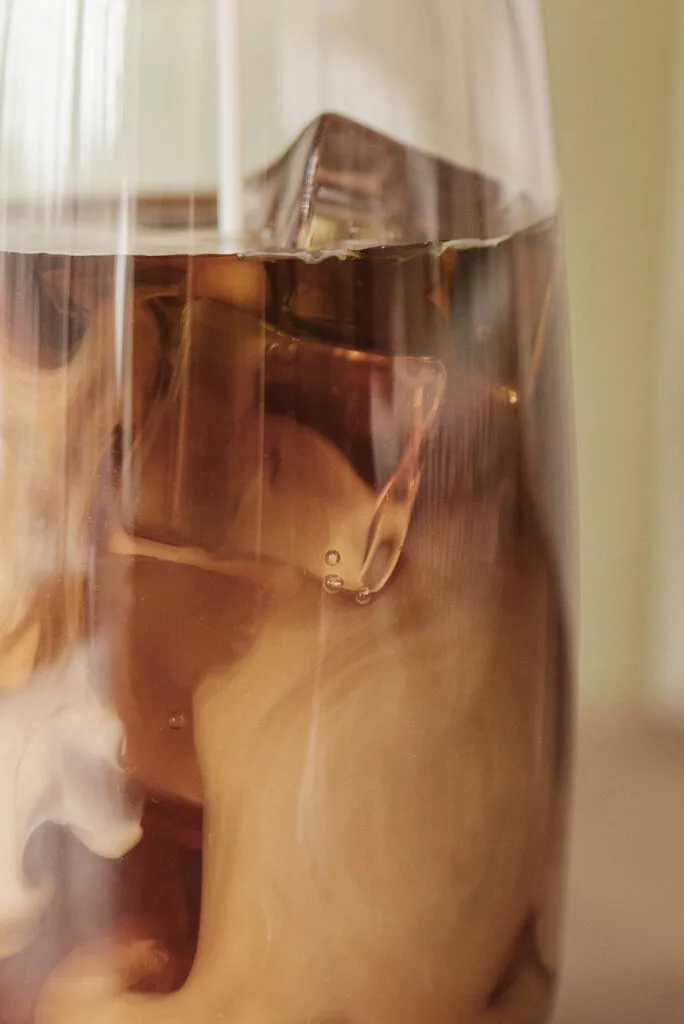 A glass of coffee with ice cubes in it.