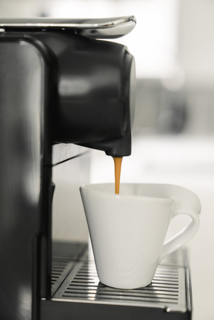 A cup of coffee is being poured into an espresso machine.