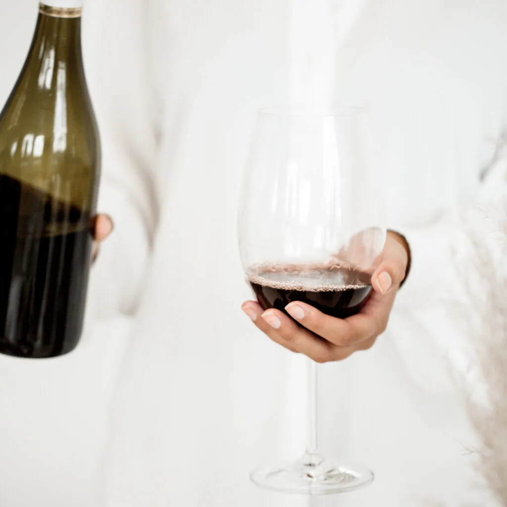 A woman holding a glass of red wine and a bottle of wine.