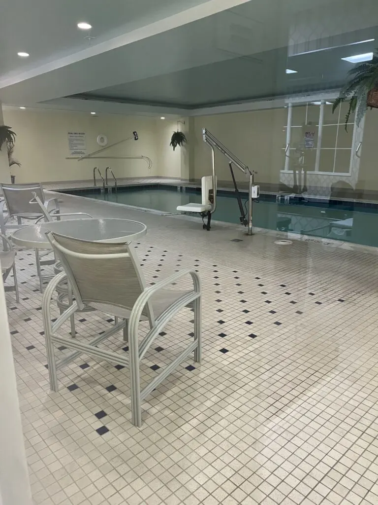 A luxurious  hotel indoor swimming pool with comfortable chairs and a sleek table.