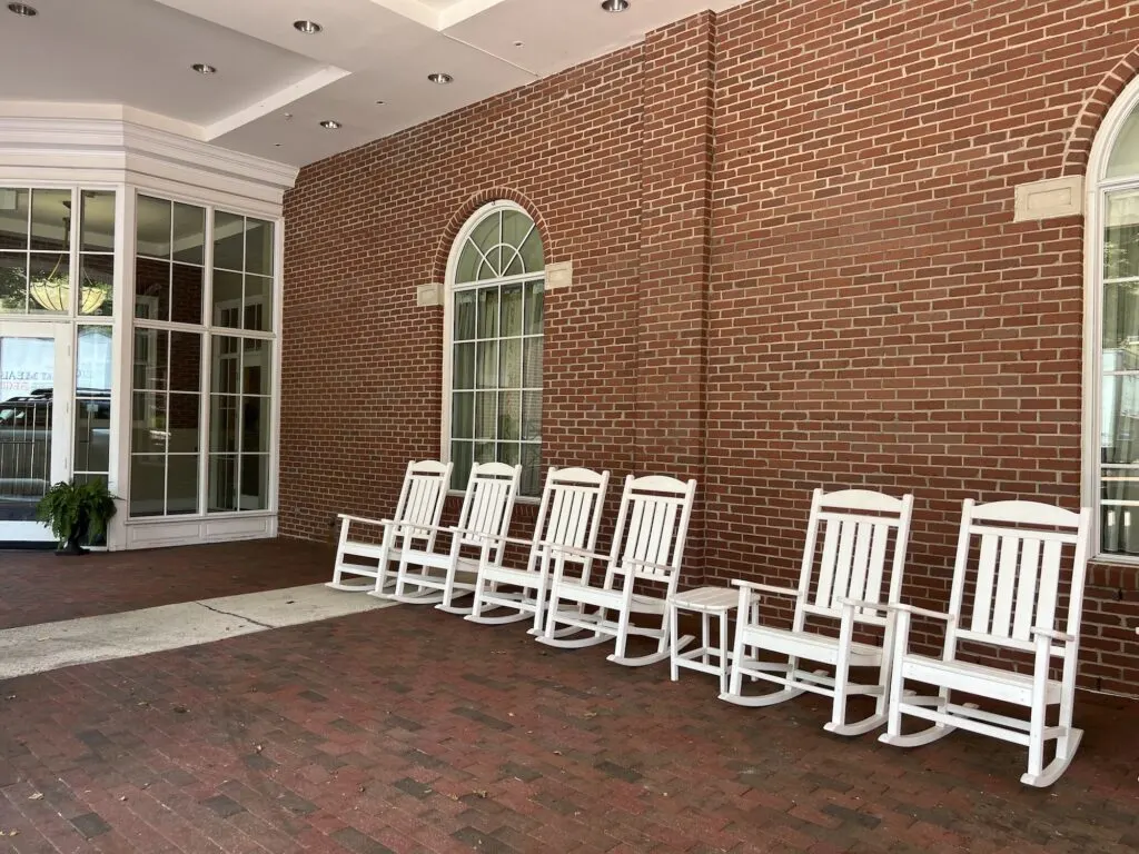 A row of white rocking chairs in front of a hotel.