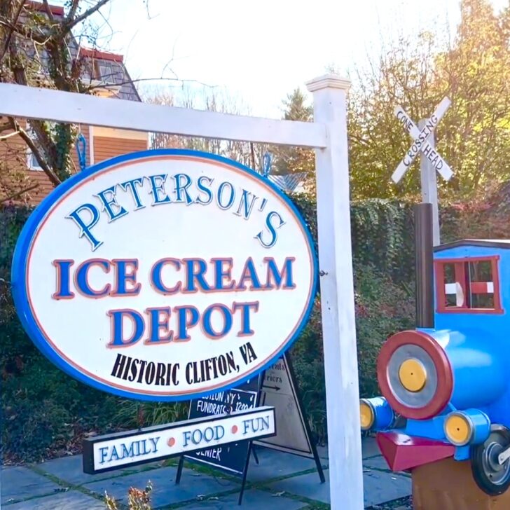 A sign for Peterson's Ice Cream Depot in Clifton VA stands next to a blue and red toy train structure on a sunny day.