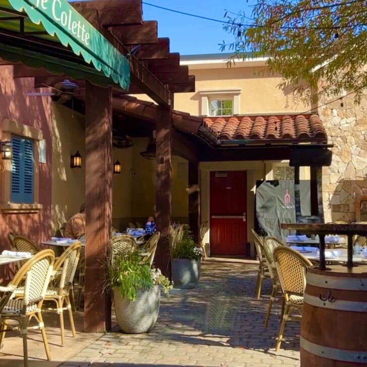 Outdoor caf&eacute; patio with wicker chairs and tables, shaded by a wooden pergola and surrounded by potted plants and stone buildings&mdash;a perfect spot if you're wondering where to eat in Clifton VA on a sunny day.